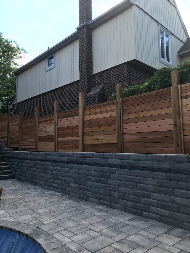 Segmental block retaining wall with horizontal cedar privacy fence above a paver patio