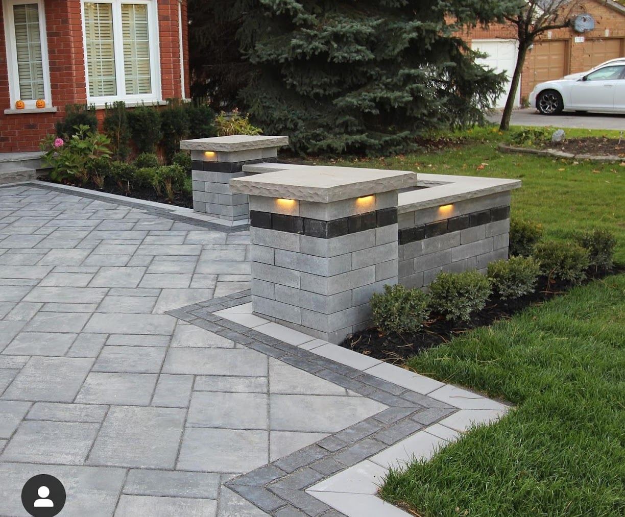 Paver driveway entry with lit masonry stone pillars and boxwood hedging
